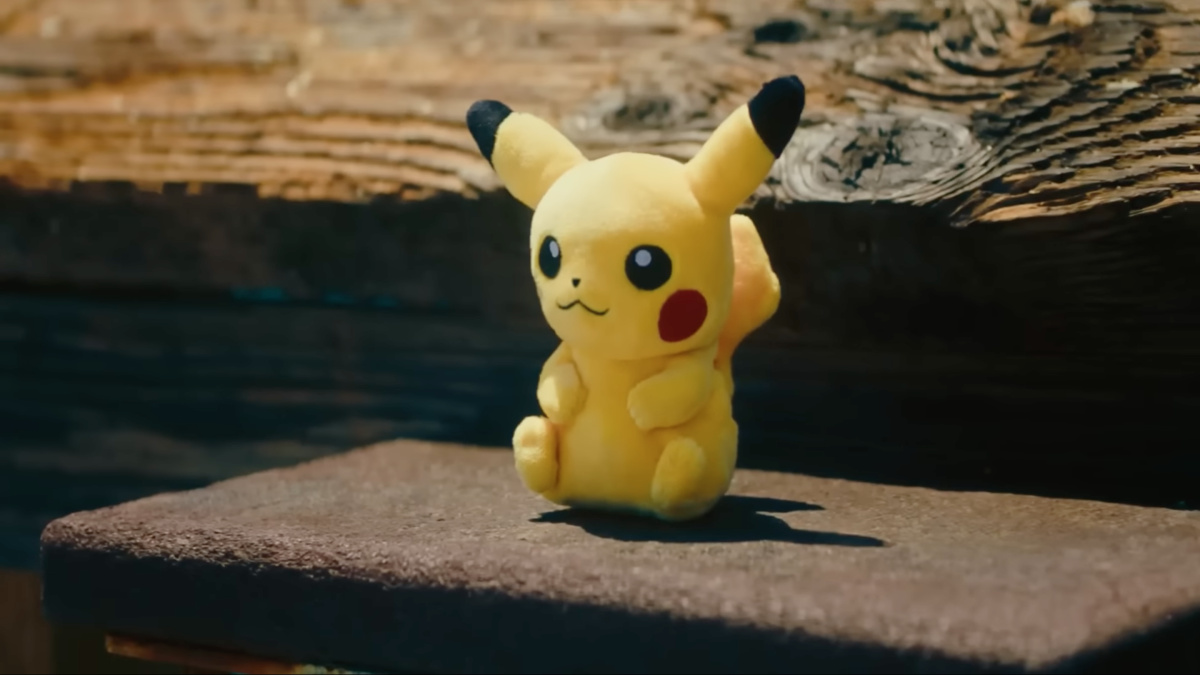 A photograph of a Pikachu plush toy on a bench on a bridge.